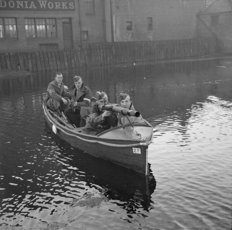 Figure 2 — Home Guards patrolling a canal in Edinburgh in a motor boat armed with rifles and a Lewis gun, 19 October 1940. The Lewis in the bows is an aircraft-pattern gun without a radiator casing. War Offic…