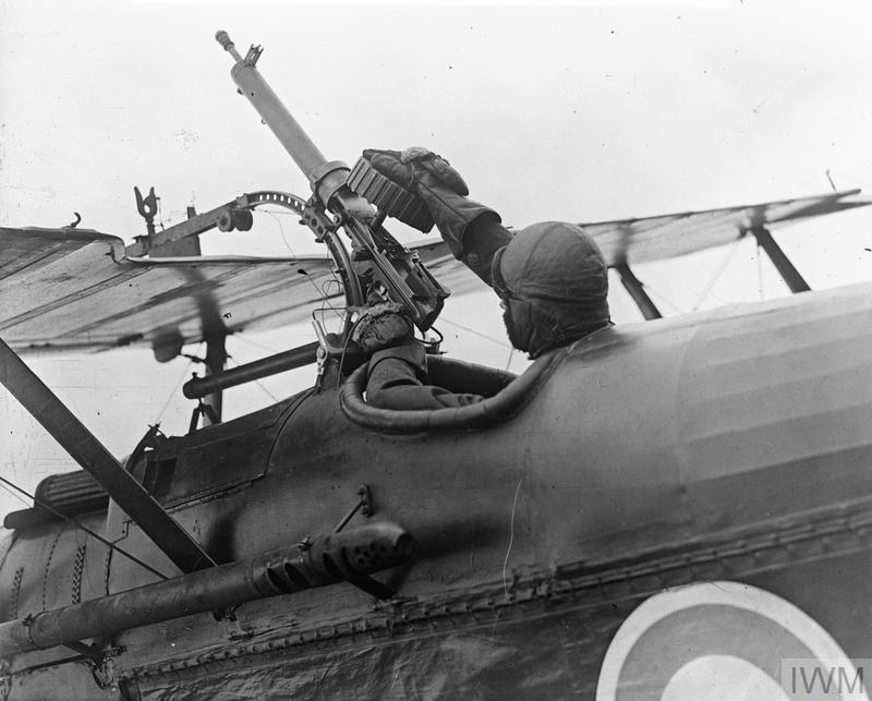 Figure 3 — The pilot of an S.E.5a of No. 1 Squadron putting a fresh double drum on the Lewis gun on the upper plane of his aircraft, Clairmarais aerodrome, 3 July 1918. The gun sits on a sliding mount above t…