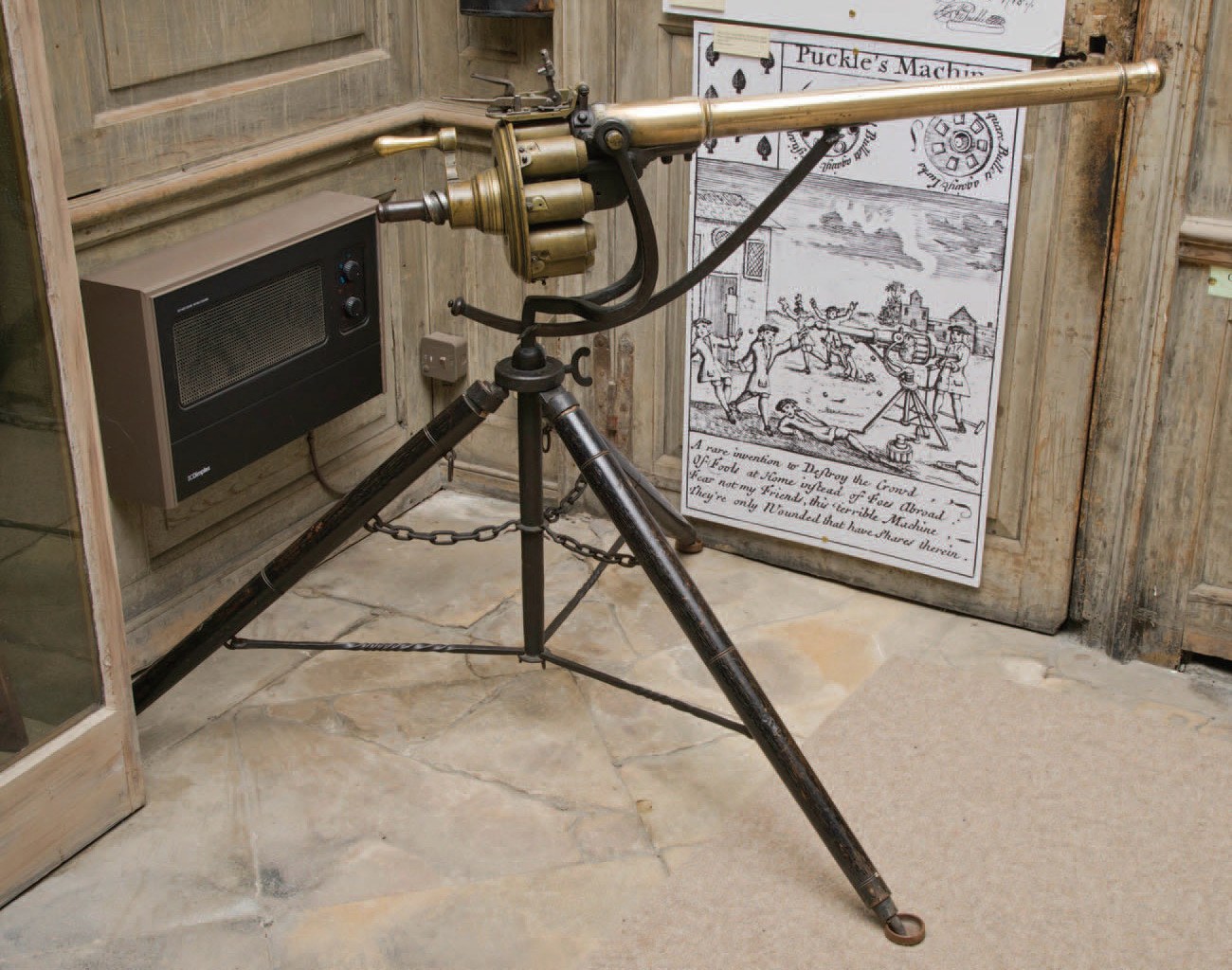 Figure 2 — The Puckle gun at Boughton House, in the collection of the Duke of Buccleuch and Queensberry. Brass barrel and chamber set on an iron tripod, with chain and stretchers; behind it hangs a large copy…