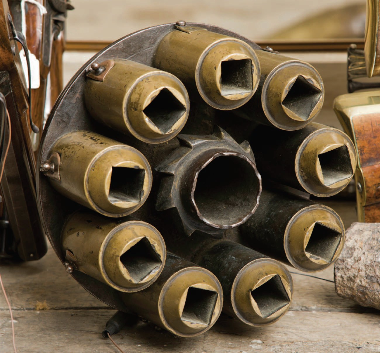 Figure 3 — A spare chamber set ("charger") for the Boughton gun, seen from the muzzle end. Nine brass tubes, each bored square with a chamfered mouth, are fixed round a hollow iron centre that carries a ring …
