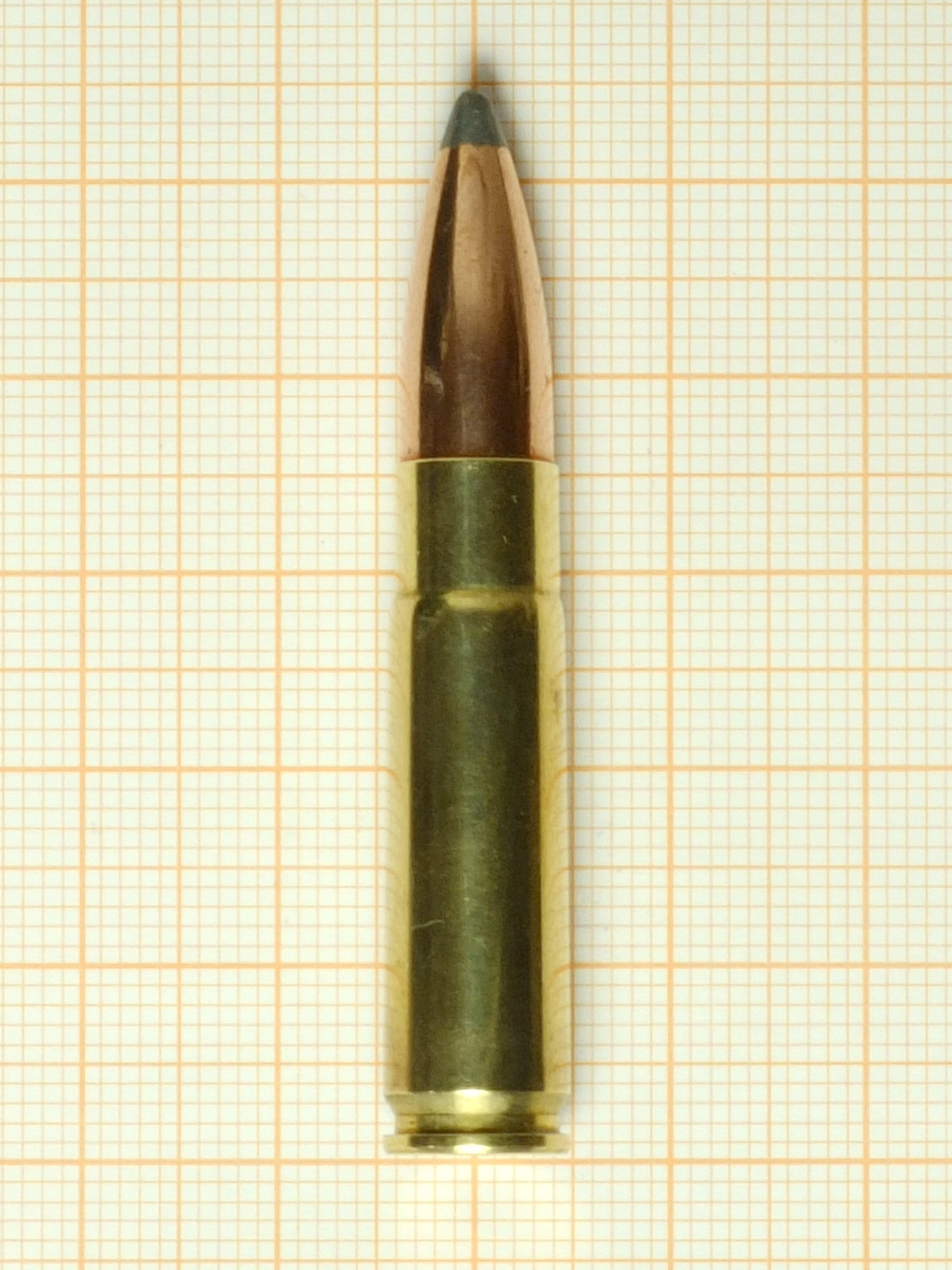 Figure 1 — A single .300 AAC Blackout cartridge photographed against graph paper, which gives the scale better than any caption can. The case is a 5.56 case shortened and opened up at the neck to take a .308-…