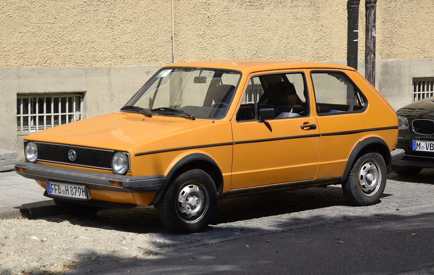 Figure 2 — A first-generation Volkswagen Golf, 1974. The folded-paper era of Giugiaro's car work — flat planes, hard creases, a single unbroken shoulder line — is the visual grammar that the Neos's long flat-…