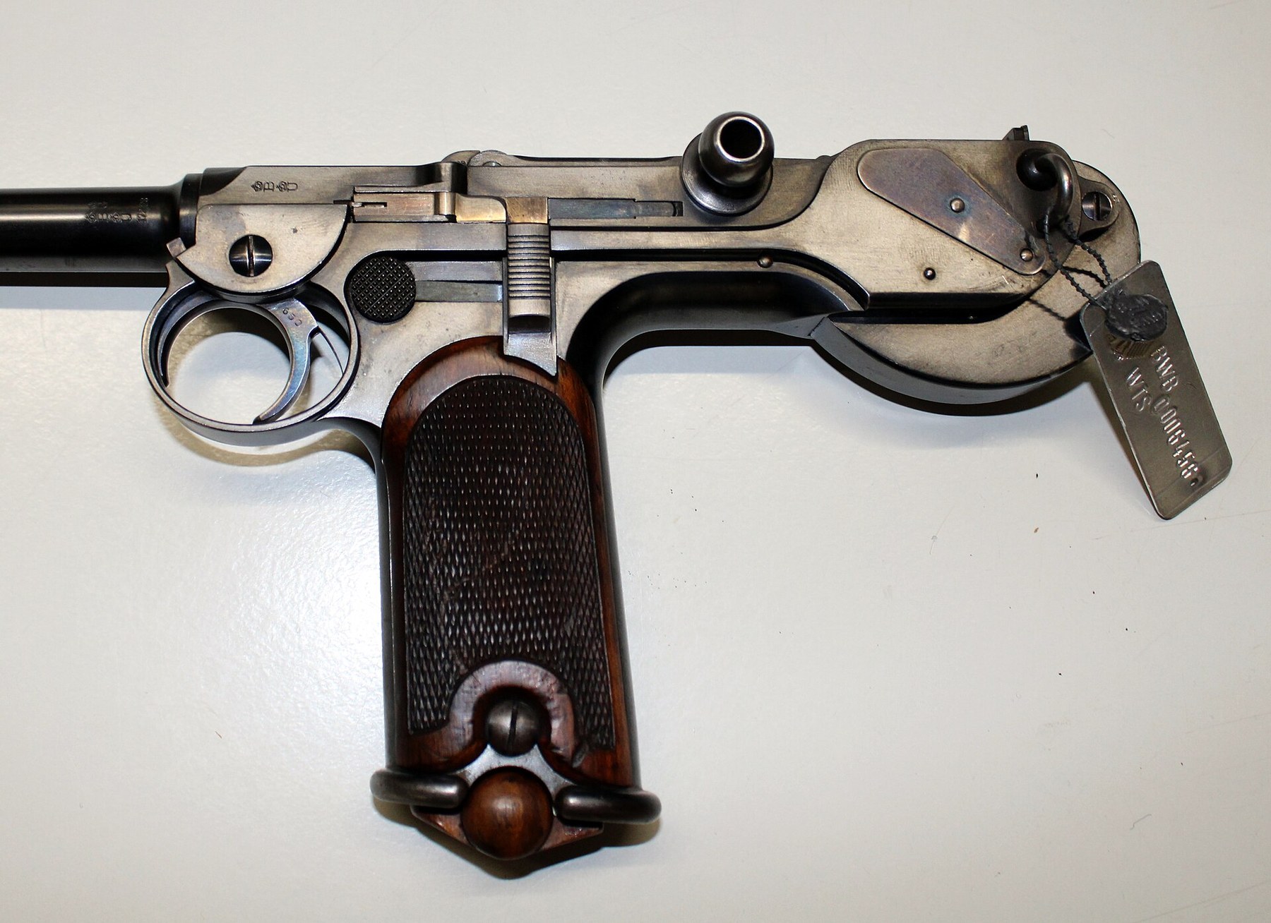 Figure 13 — The left side of the Loewe pistol's action. The toggle knob stands at upper centre; the serrated vertical piece above the front of the grip panel is the safety slide; the chequered disc nearer the …