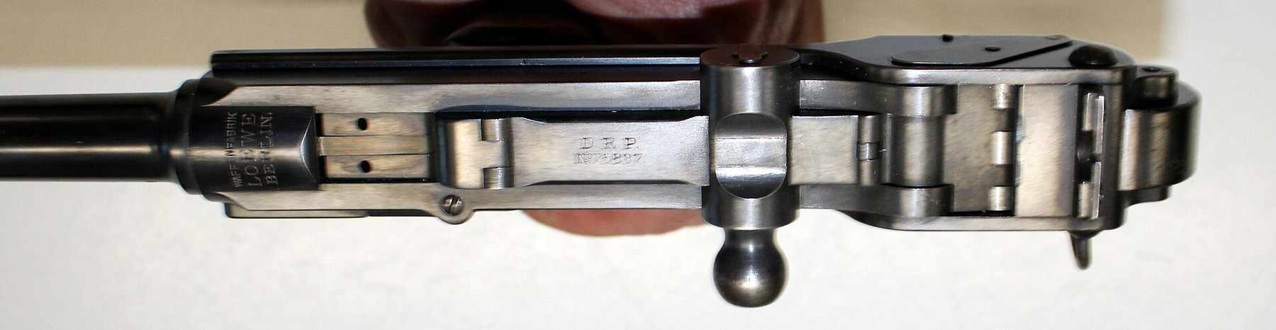 Figure 16 — The action of the Loewe pistol from above. The chamber top carries the Loewe maker's marking; behind it, the breechblock lies between the two arms of the forked receiver; the toggle top carries "D.…