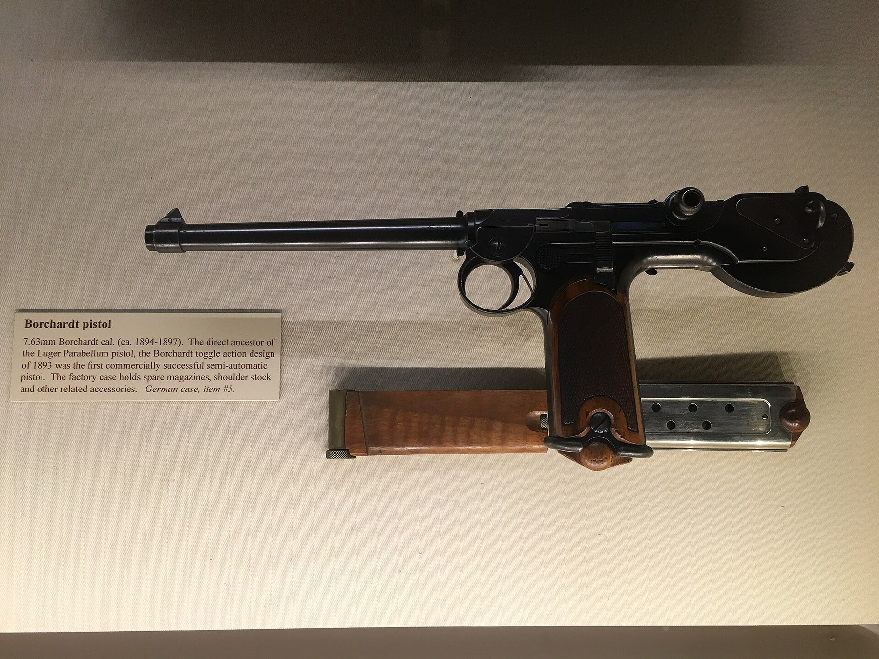 Figure 5 — The C-93 at the NRA National Firearms Museum. Below it lie a spare magazine, right, and the magazine-shaped wooden barring block with the brass cap of its oiler, left. The label calls the pistol th…