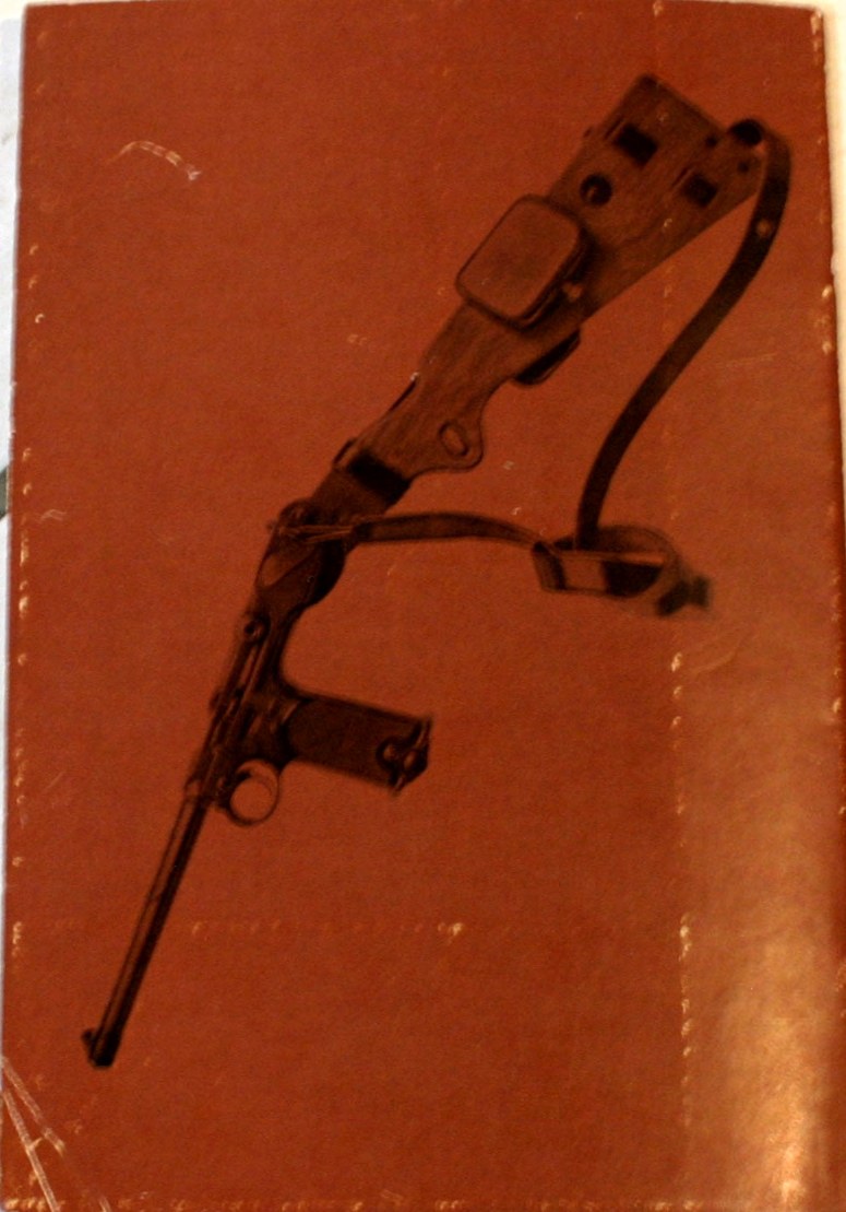Figure 5 — The back cover of the DWM English manual, showing the pistol with its board stock fitted, the leather holster laced to the stock, and the shoulder strap. The factory sold the C-93 as a pistol that …