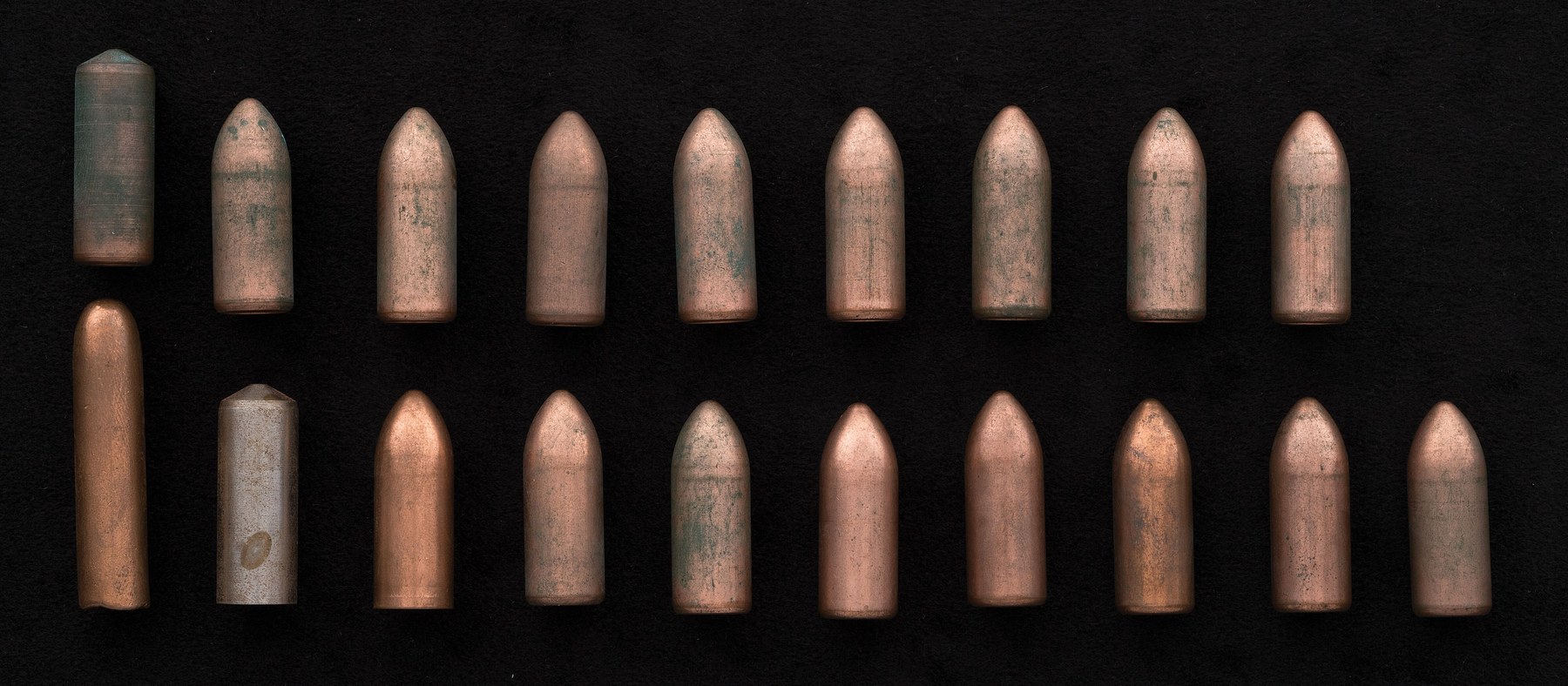Figure 7 — A mixed lot of 13 mm rounds: fifteen full-metal-jacket pattern rounds, a semi-wadcutter, and two fired cases whose nozzle plates have been removed. Rock Island Auction Company photograph, used by o…