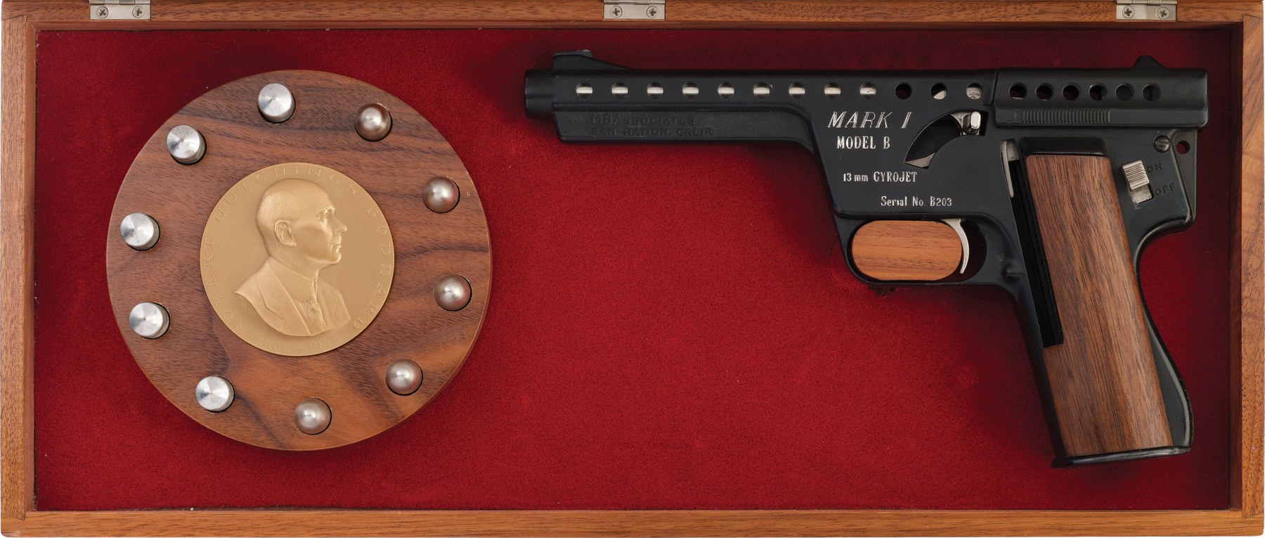 Figure 12 — A Mark I Model B presentation set of the kind Rock Island dates to about 1965–66: the black pistol, the walnut case lined in red felt, the Goddard medallion ringed by dummy rounds. This set, with i…