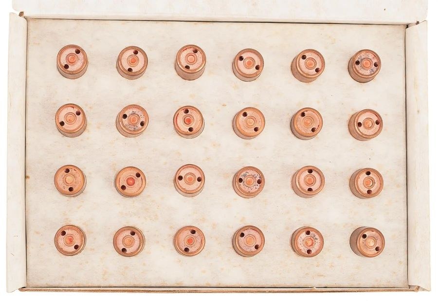 Figure 3 — Twenty-four 13 mm rounds with the later two-port bases, a change Carpenter traces to a machine that could drill two ports at once, bought for the flare programme. A red tint shows round several pri…