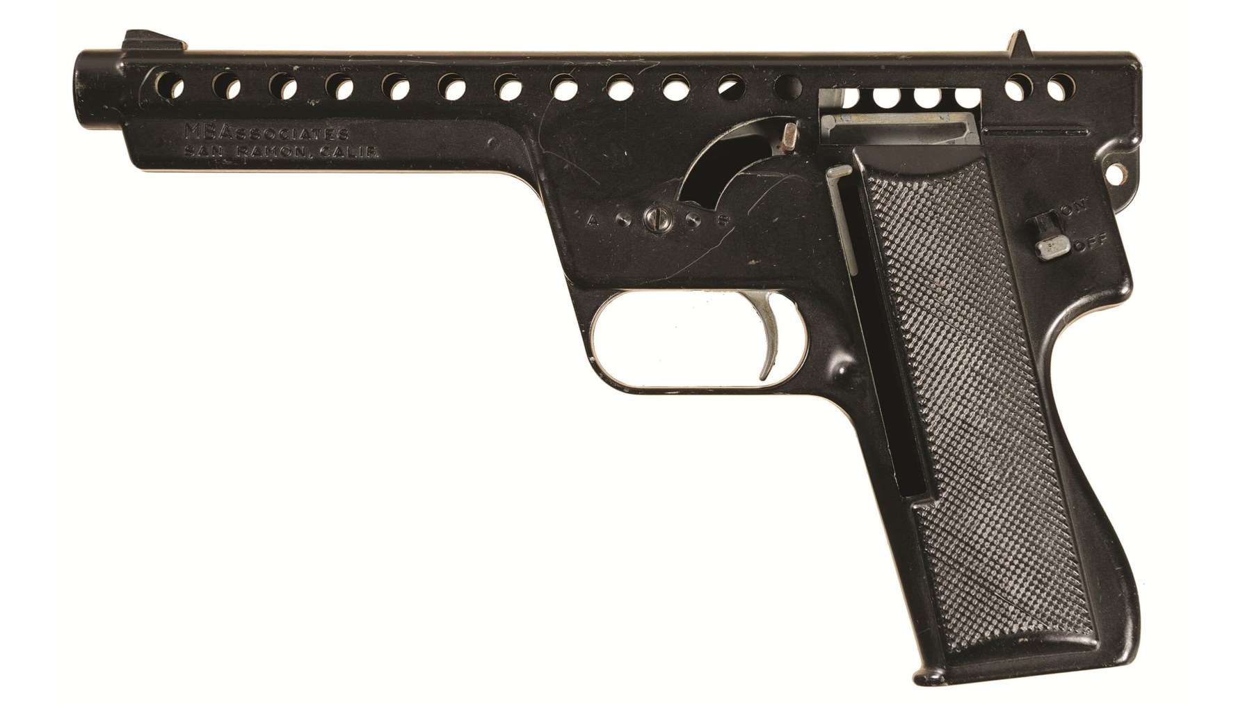 Figure 4 — A Model 137 from the left: the one-piece cast frame with cast-in grip checkering, the MBAssociates San Ramon address on the lug, a continuous top line with no rear slide, and the plugged selector b…
