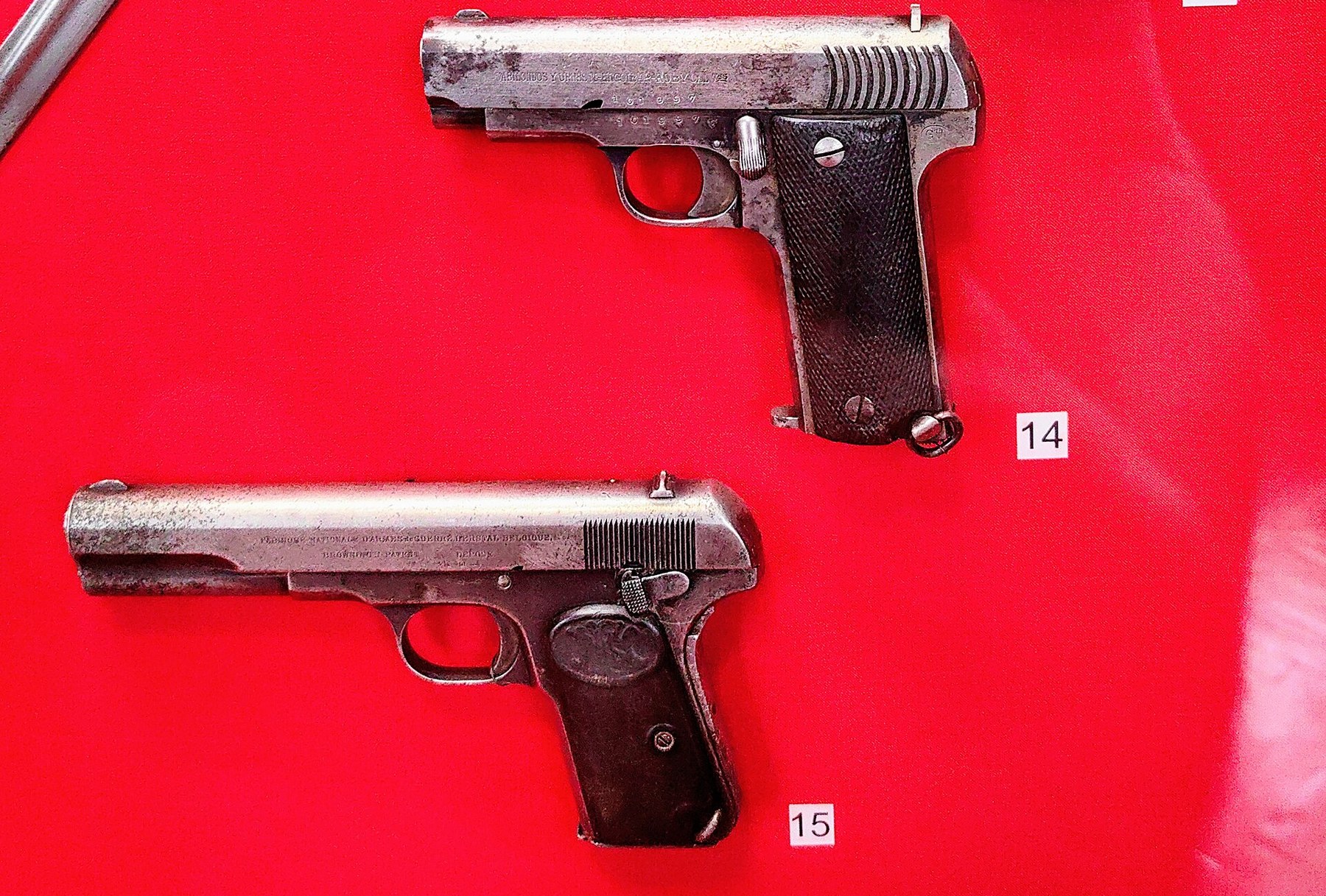 Figure 2 — A Ruby above a Browning: in the New Castle at Hrodna, a Gabilondo Ruby (14), whose slide reads GABILONDOS Y URRESTI, ELGOIBAR, RUBY, CAL 7.65, hangs above an FN Model 1903 (15). The family likeness…