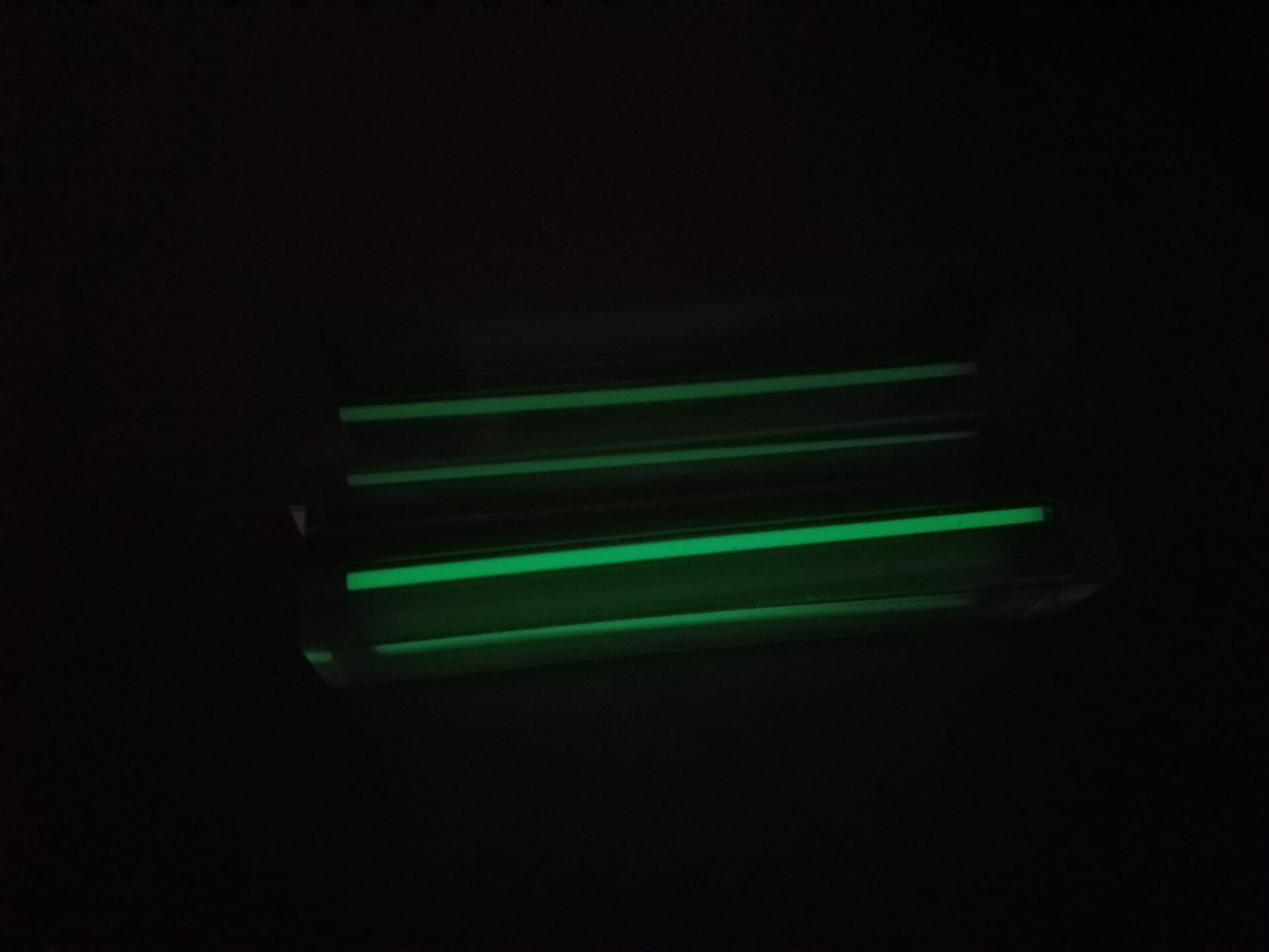 Figure 4 — Two tritium vials of the same size cast in acrylic and photographed together: the upper one is 50 GBq, the lower one 200 GBq. Four times the activity is visibly brighter. The brightness of a tritiu…