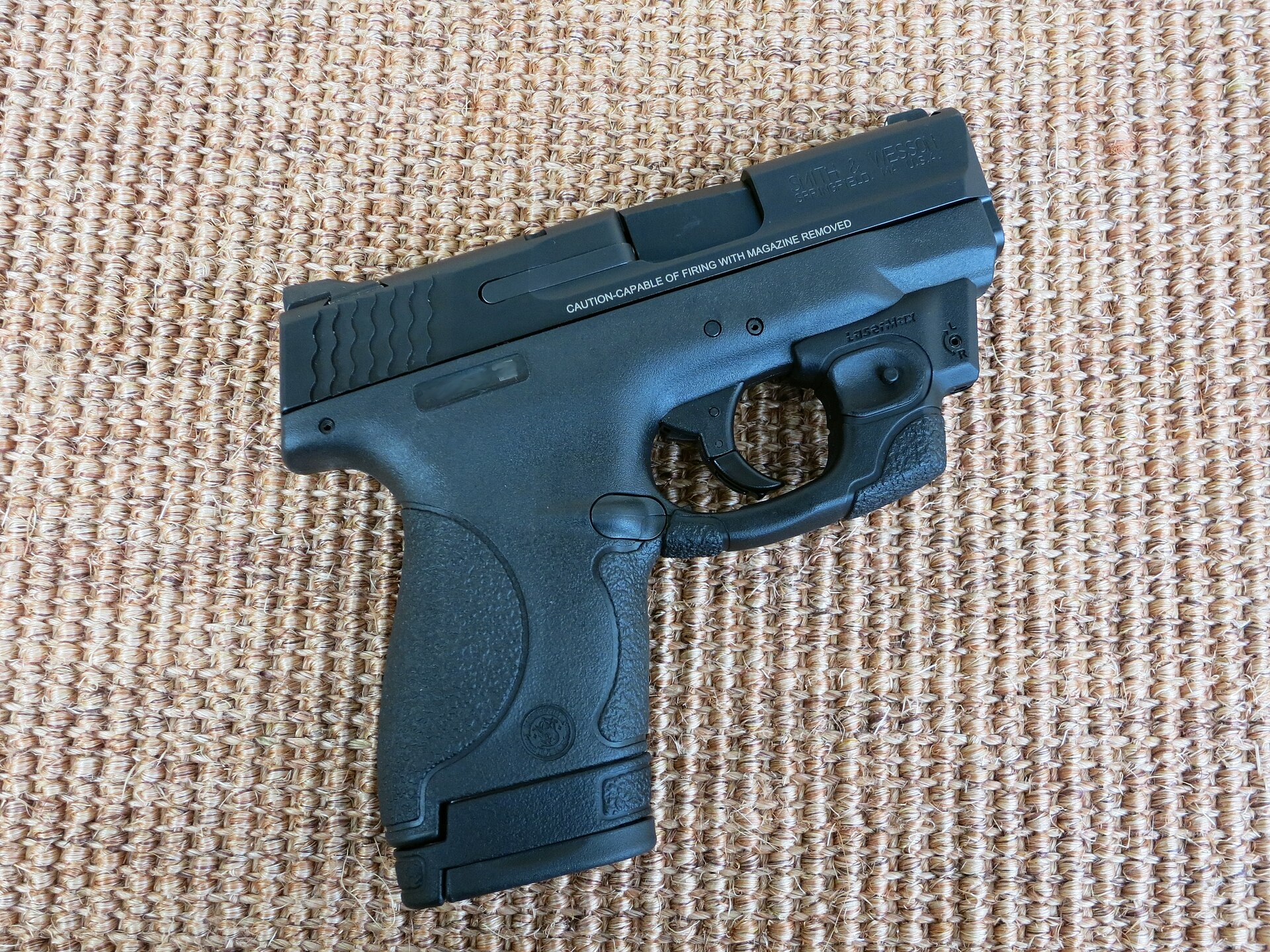 Figure 3 — An original-pattern 9 mm Shield, photographed in December 2015, fitted with an aftermarket trigger-guard laser (a LaserMax, according to the photographer) and the 8-round extended magazine with its…