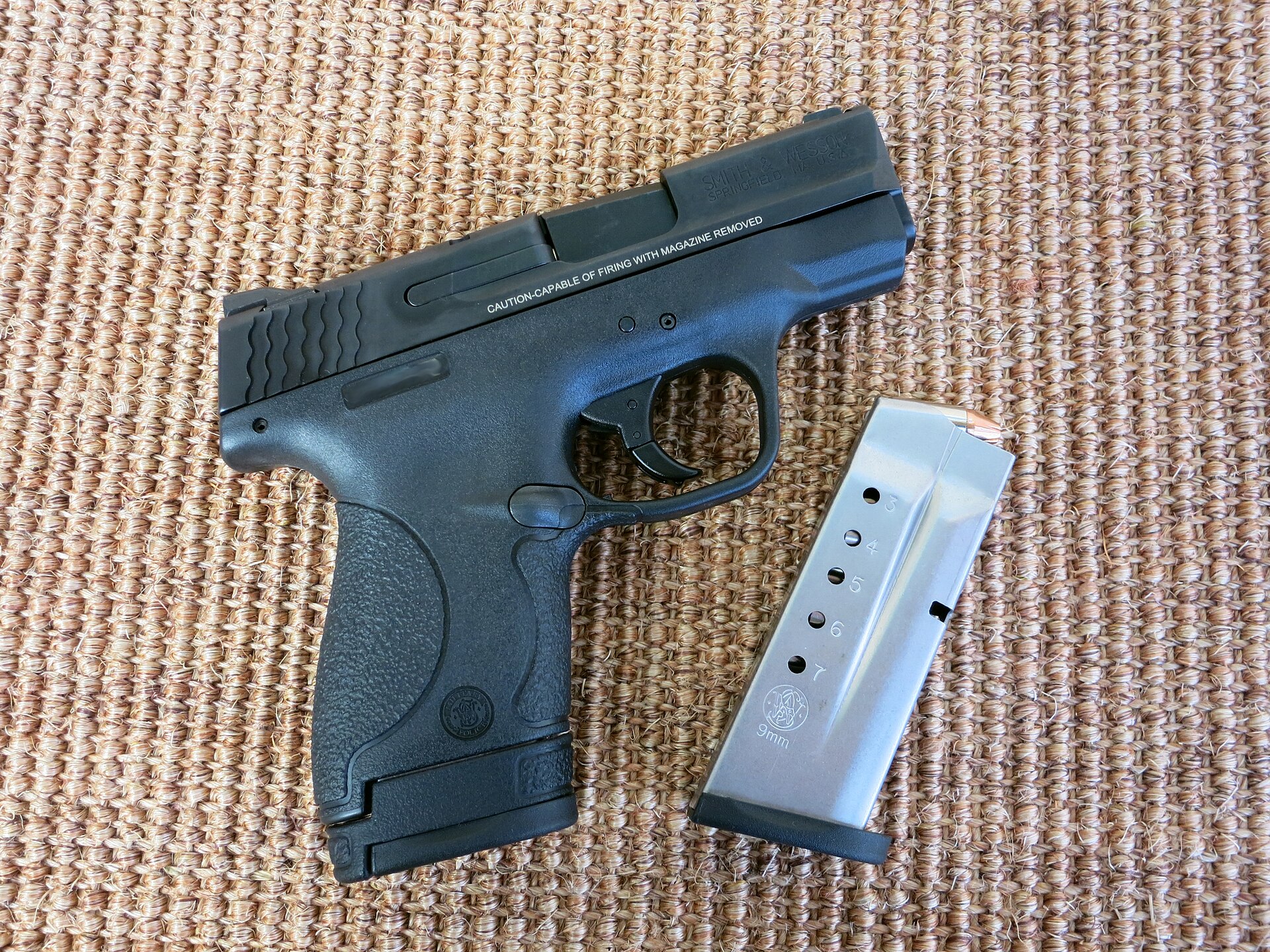 Figure 1 — An original-pattern Smith & Wesson M&P Shield in 9×19, photographed in January 2015, with the 8-round extended magazine inserted and the 7-round flush magazine beside it. Everything that identifies…