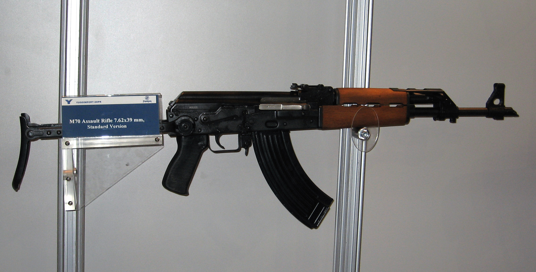 Figure 4 — A Yugoslav rifle displayed with a placard reading "M70 Assault Rifle 7.62x39 mm, Standard Version". The reinforced front end is common to the family; the stock is what the designation suffixes track.