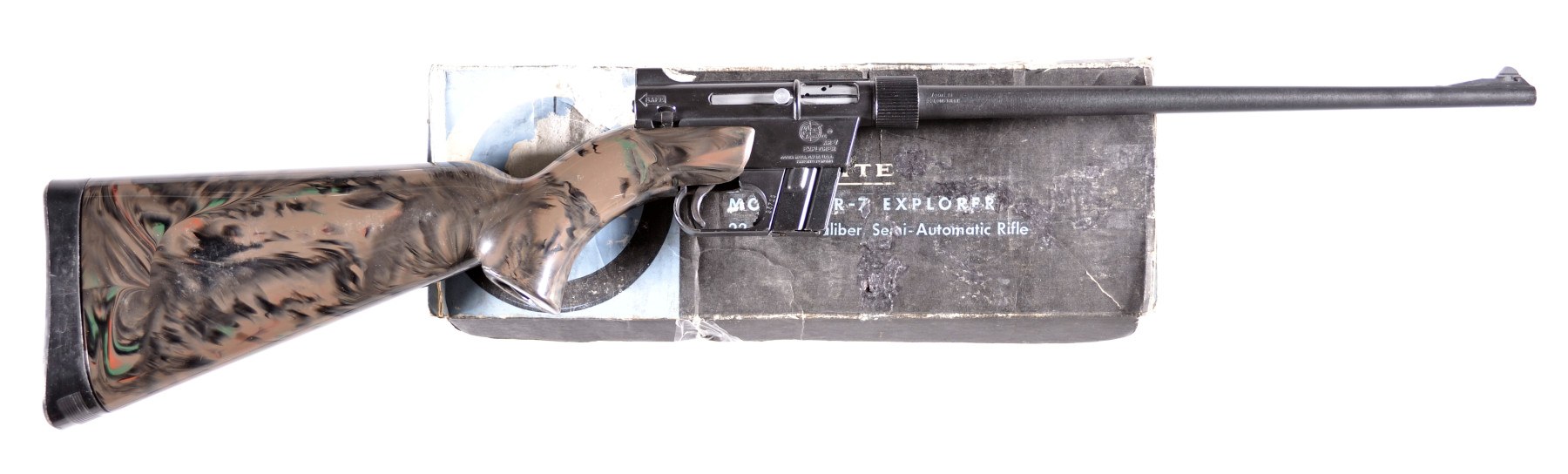 Figure 3 — An ArmaLite AR-7 with a swirled stock in front of its original box, printed "Model AR-7 Explorer" and "Semi-Automatic Rifle". The left side of the receiver carries the ArmaLite roundel. Rock Island…