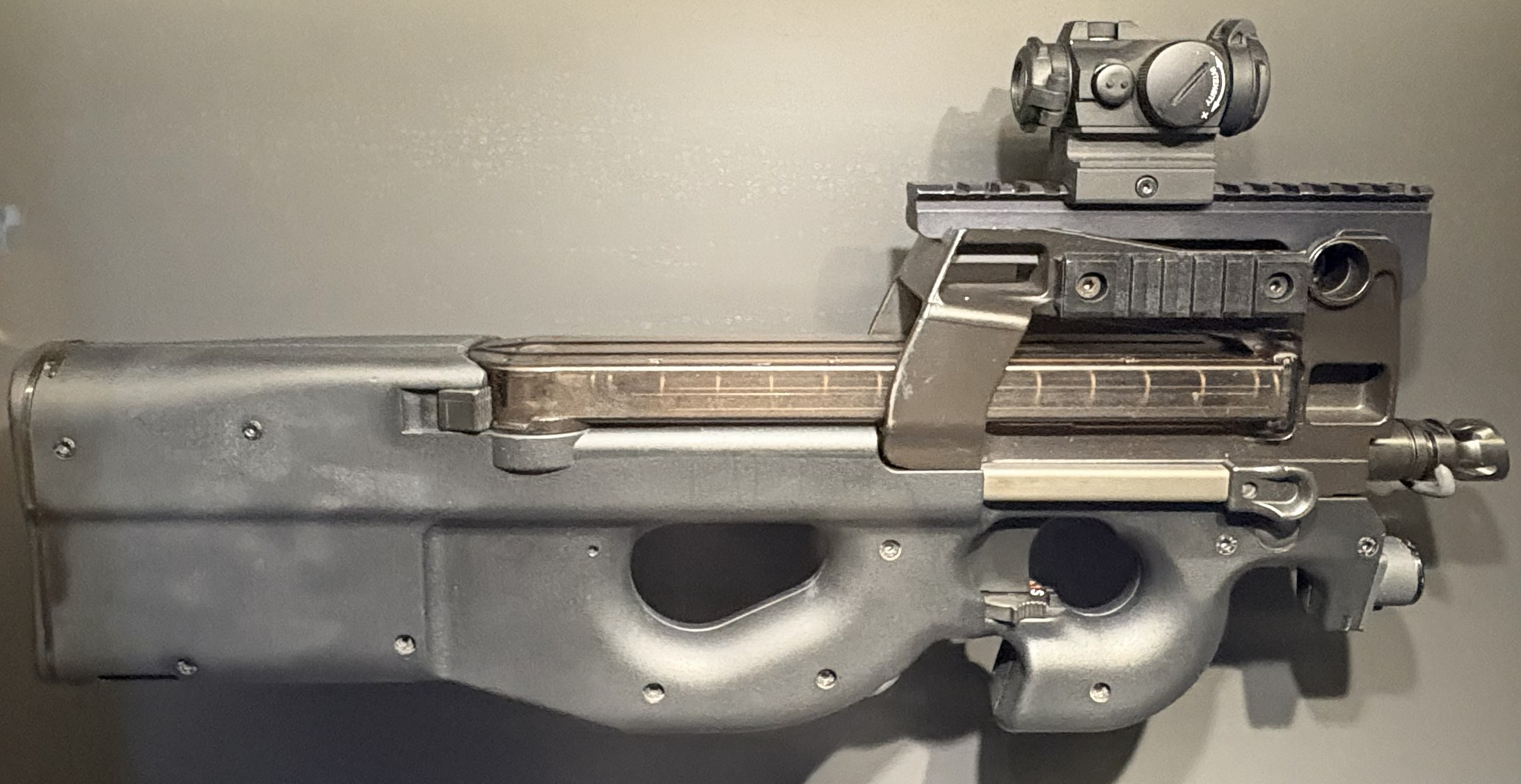 Figure 14 — A detail view of a rail-equipped P90 with a red dot fitted. The translucent magazine running beneath the optic is visible here, which is the clearest illustration of why the sightline sits as high …