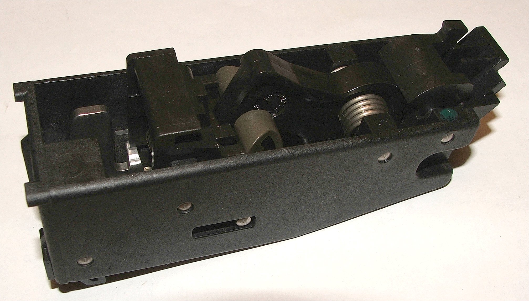 Figure 4 — The PS90's hammer group, removed from the frame. The fire-control components live at the rear of the weapon, behind the shooter's hand — which is precisely why the trigger has to reach them through…