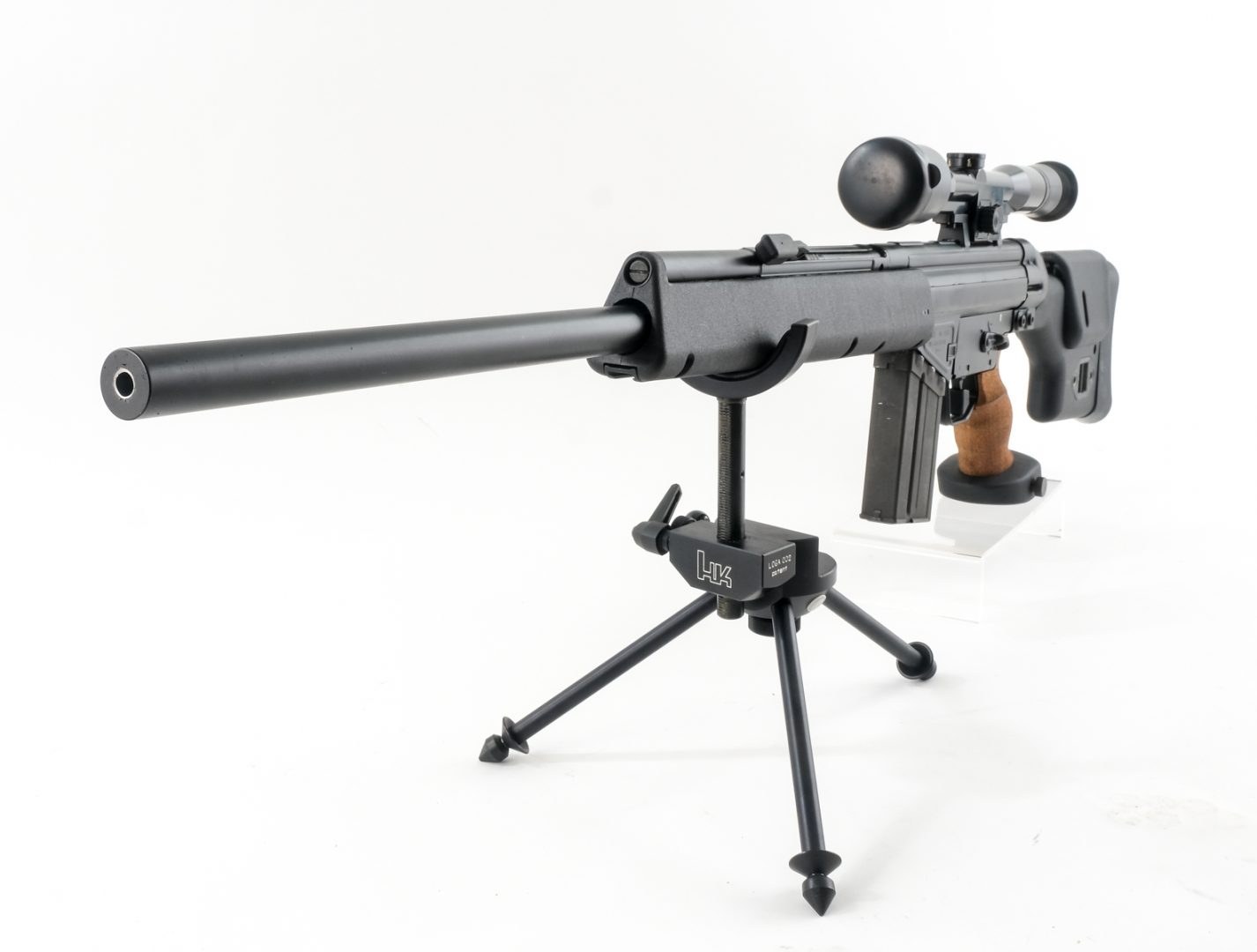 Figure 7 — A PSG1 on an H&K-branded precision tripod: the tripod head is engraved "LOGA 002", and its yoke cradles the handguard from below; a threaded column sets the height. Photograph by CT Firearms Auctio…