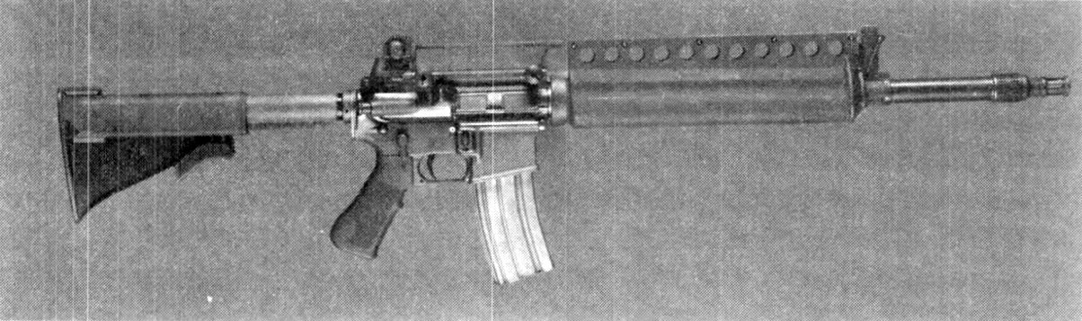 Figure 5 — Colt's Advanced Combat Rifle with iron sight, as photographed for the US Army in 1989: an M16A2 derivative with a telescoping stock, a ventilated handguard and a muzzle brake compensator, firing du…