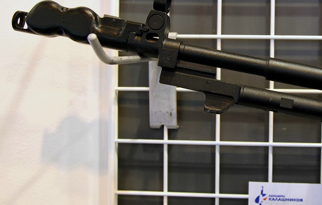 Figure 8 — Close-up of an AN-94's front end at an exhibition: the open, looped muzzle device that Russian sources describe as a self-cleaning brake, the hooded front sight, and the guide rod running under the…
