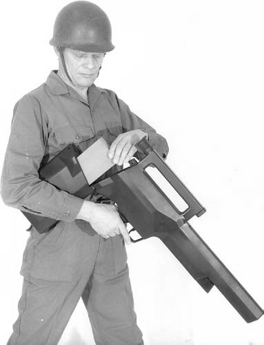 Figure 7 — A caseless light machine gun from the same programme, shown in a period photograph with a 300-round ammunition box being loaded into the stock, as the file's description puts it. Photograph credite…