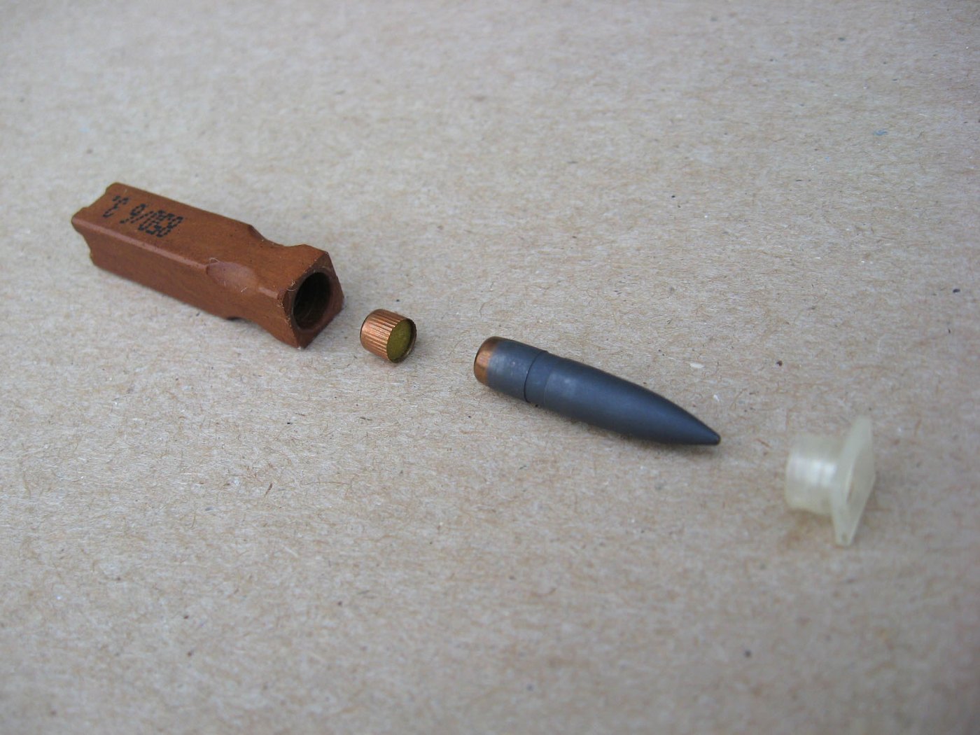 Figure 4 — The 4.73 × 33 mm caseless round taken apart, left to right: the moulded propellant block, the primer, the bullet, and the plastic cap that centres the bullet in the block. Photograph: Drake00 at En…