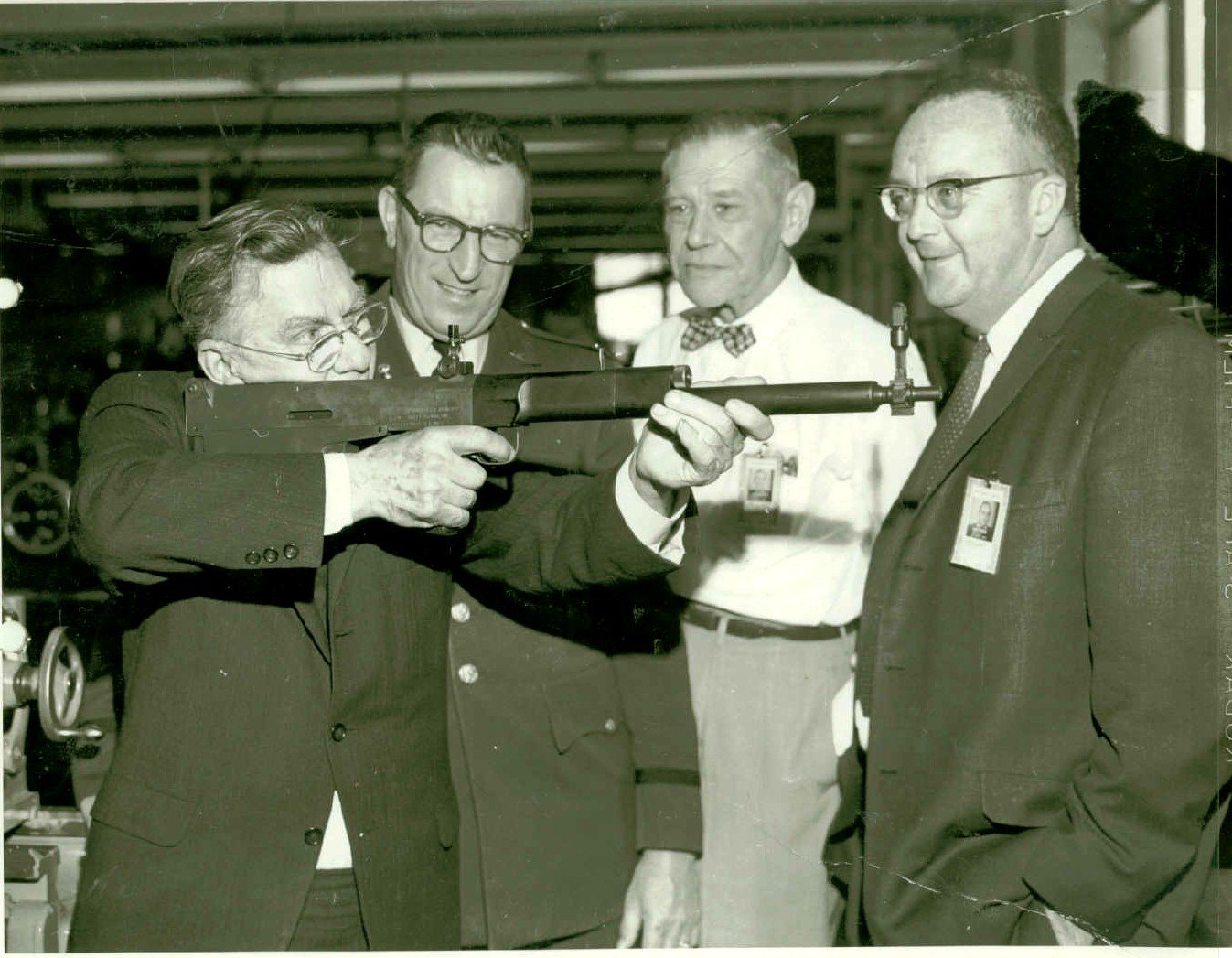 Figure 7 — Garand in April 1962, nearly a decade after he retired, shouldering an experimental bullpup at Springfield Armory. The Wikimedia Commons file names this his "T31 Bullpup"; the Park Service descript…