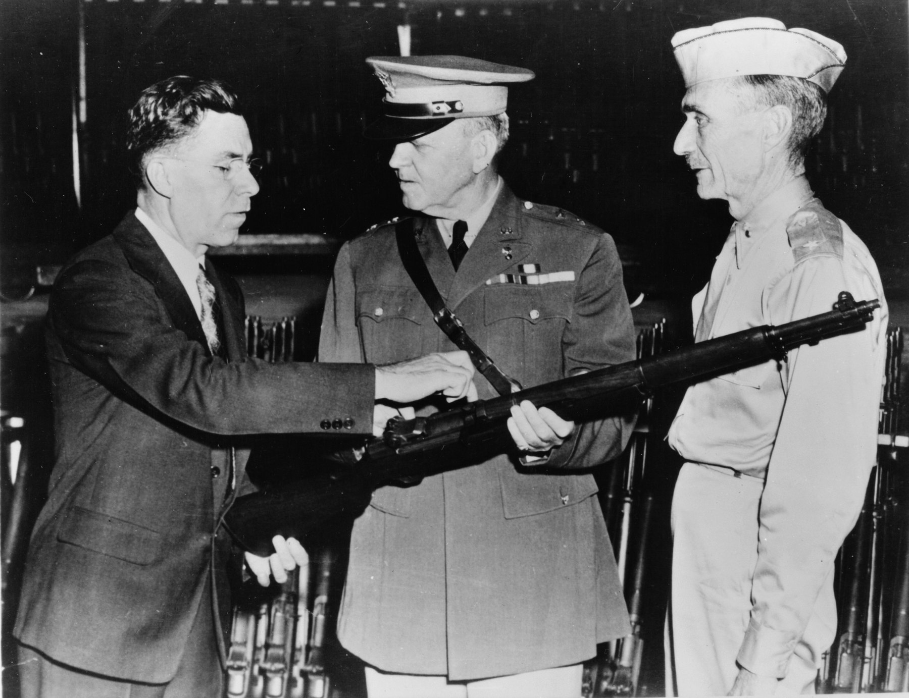 Figure 6 — Garand pointing out features of the M1 to Major General Charles M. Wesson, center, the Chief of Ordnance, and Brigadier General Gilbert H. Stewart. — Photograph: Office of War Information, public d…