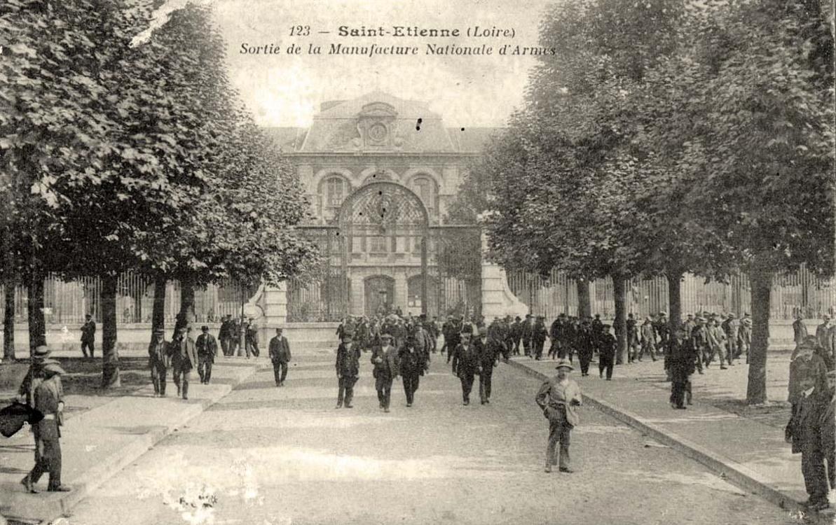 Figure 3 — Workers leaving the Manufacture Nationale d'Armes at Saint-Étienne, on a postcard of about 1900 to 1910. The gate and the clock building behind it still stand. Anonymous; public domain in the EU, v…