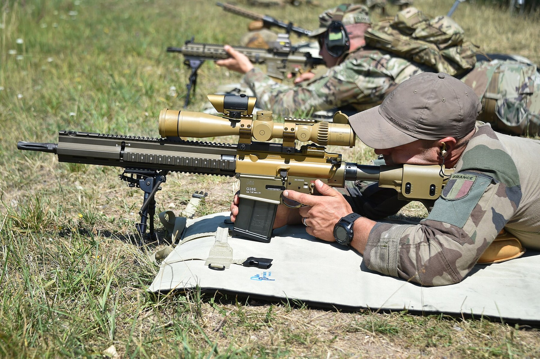 Figure 14 — A French marksman at the European Best Sniper Team Competition, Grafenwöhr, 25 July 2019, firing a tan semi-automatic rifle of the FN SCAR-H type with a long scope, identified here from the photogr…