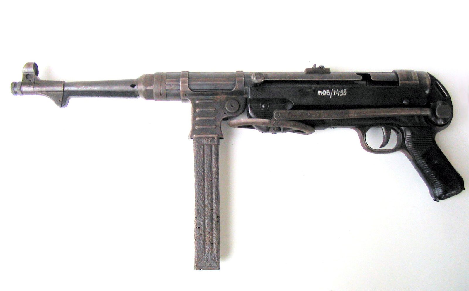 Figure 1 — An MP 40 photographed against a plain ground. Read it as a list of manufacturing processes rather than as a weapon: a rolled and welded sheet-steel receiver, a pressed magazine housing with ribs st…