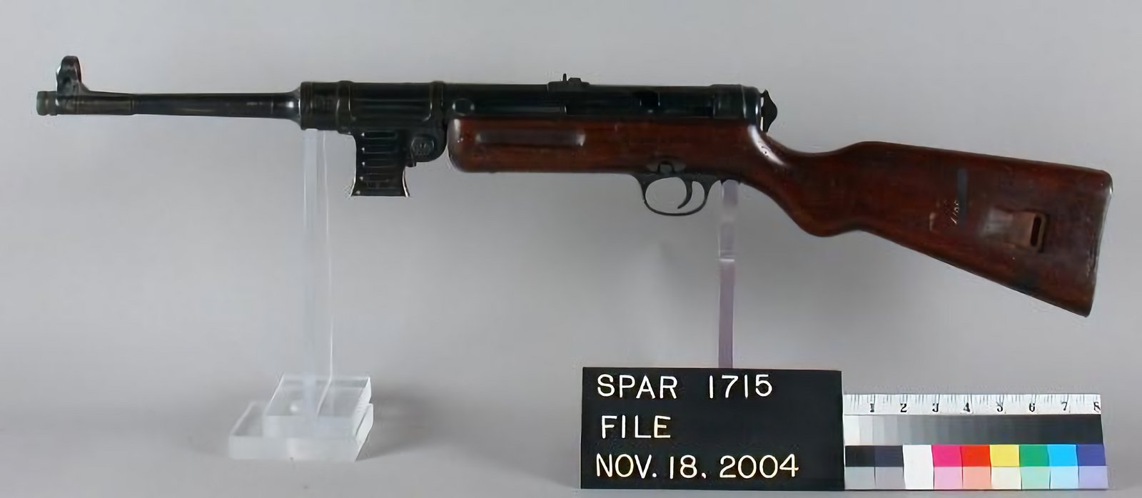 Figure 6 — An MP 41 photographed against a scale card. The wooden furniture makes it heavier and far more conventional than the weapon it borrowed its upper from, and it is one of the surest ways to distingui…