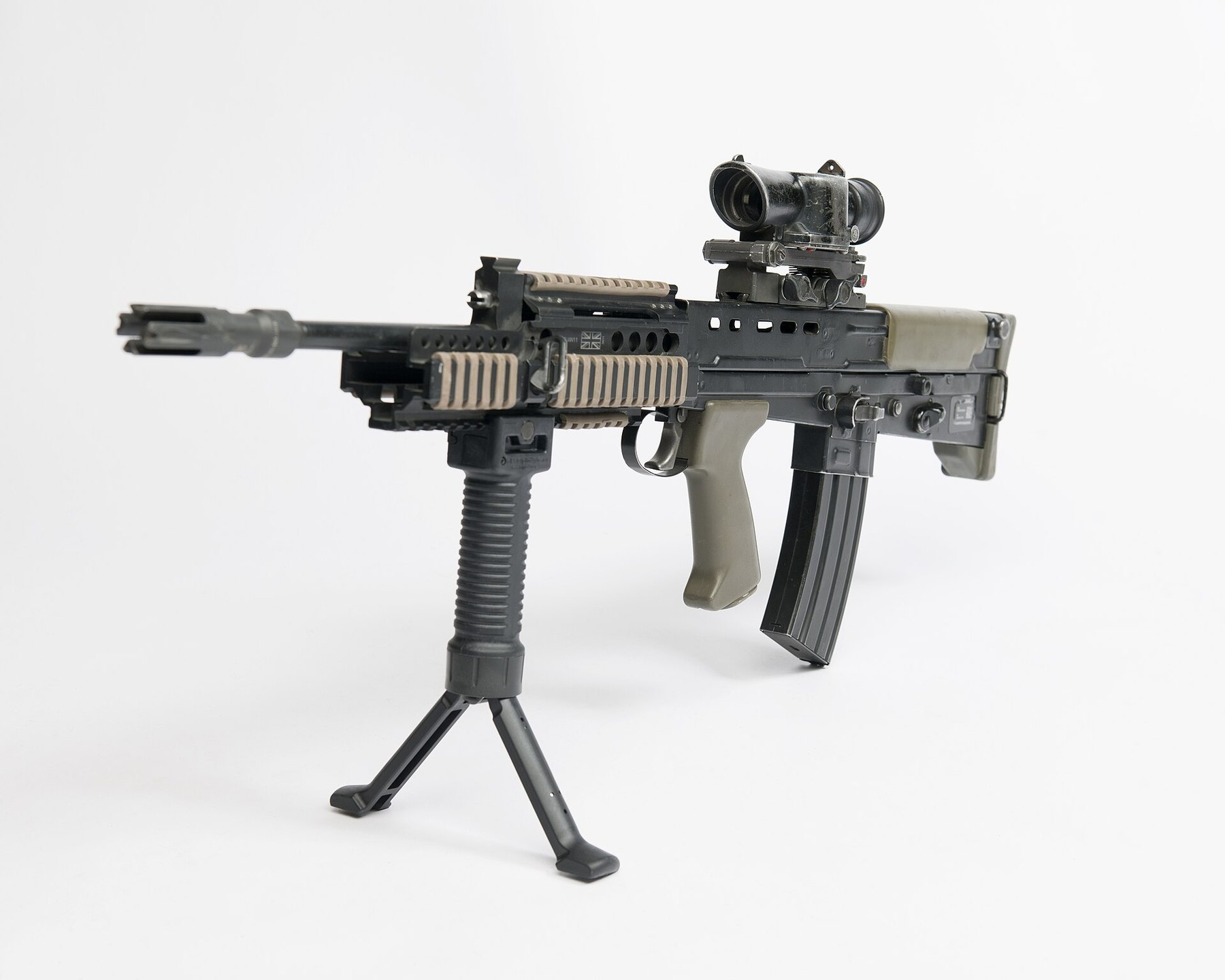 Figure 2 — An SA80-A2 with SUSAT, rail fore-end and Grip Pod deployed as a bipod, standing on its magazine and grip pod, muzzle left. MOD photograph by Stuart Hill, Open Government Licence v3.0.