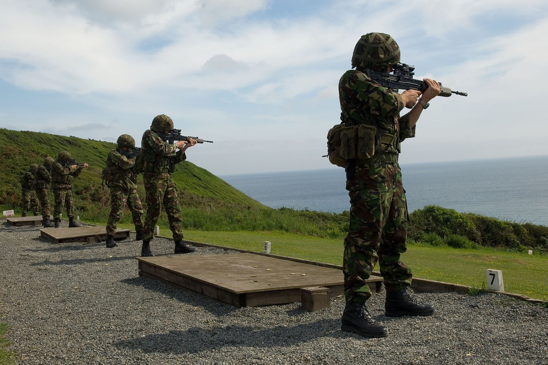 Figure 2 — A Royal Marine fires an SA80 standing on the Annual Personal Weapons Test at Tregantle Ranges, Devon, with others on the firing point behind. MOD photograph by LA(Phot) Gaz Faulkner, Open Governmen…