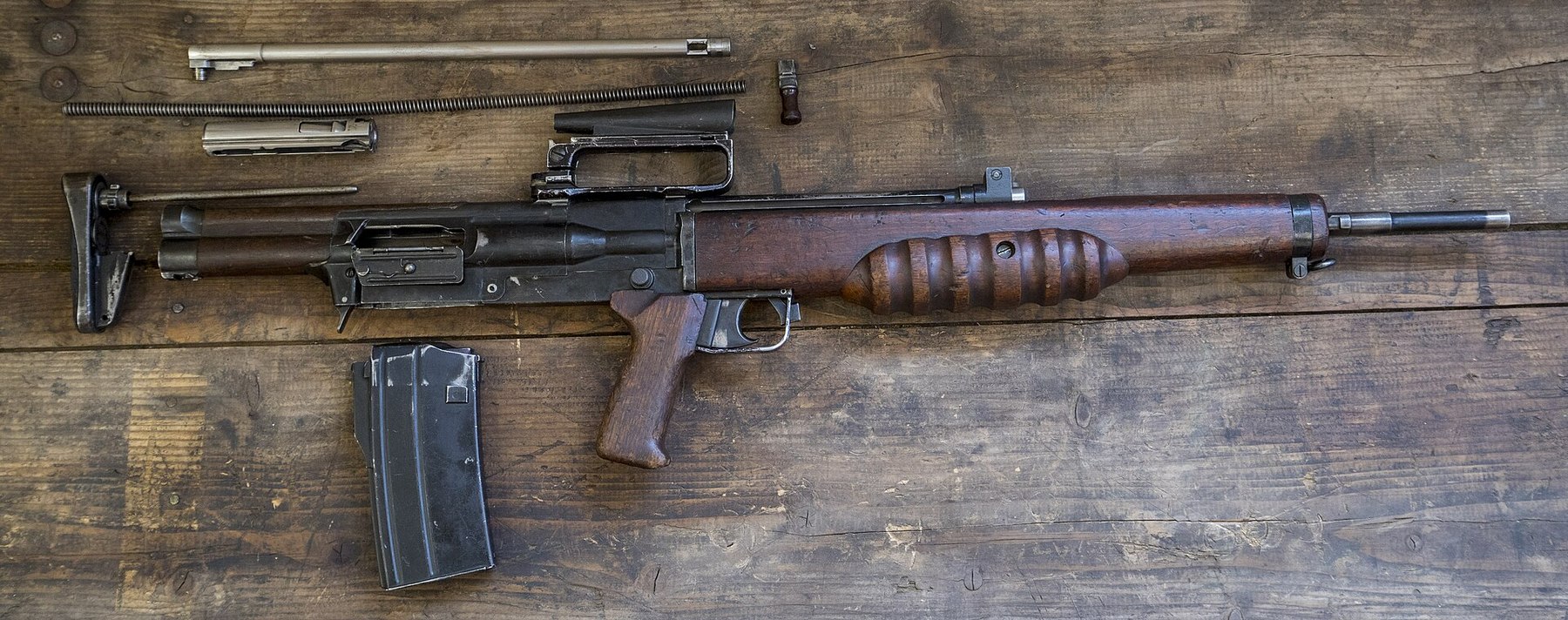 Figure 5 — The EM-2 field-stripped on a wooden bench: the wooden handguard, the receiver, the bolt and carrier, the return-spring parts and the magazine. MOD photograph by PO Phot Owen Cooban, 2016, Open Gove…
