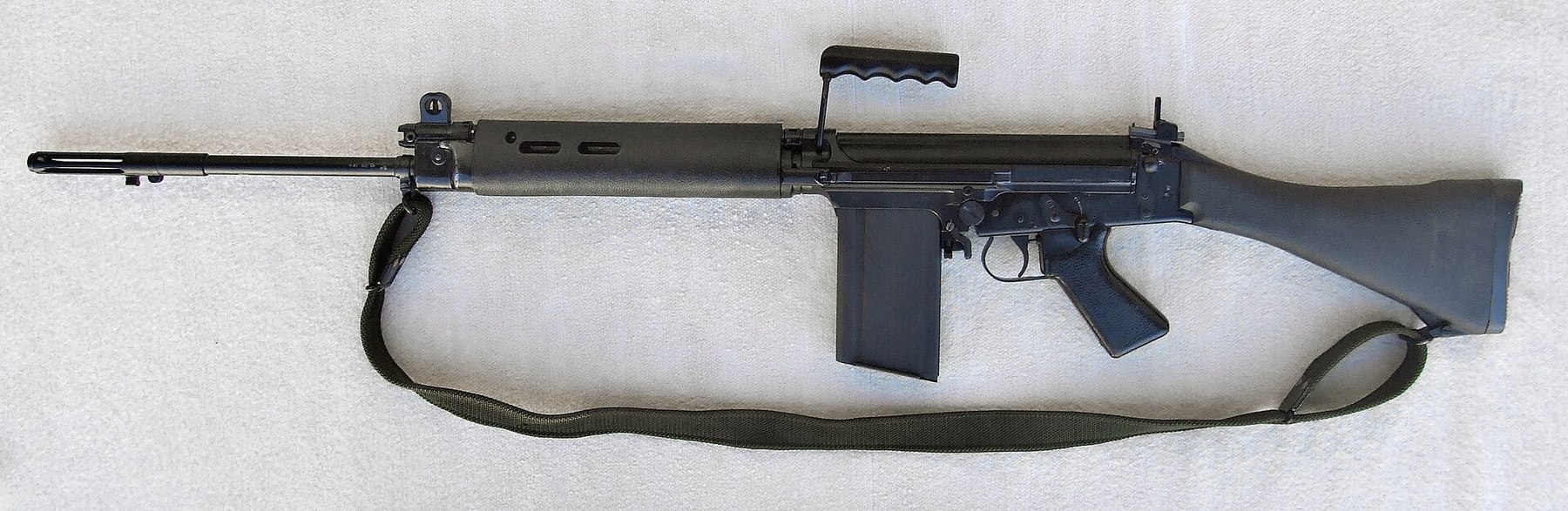 Figure 7 — An L1A1 Self-Loading Rifle on a white background, muzzle left, with its fixed wooden-patterned butt, carrying handle and 20-round magazine. Public domain, via Wikimedia Commons.