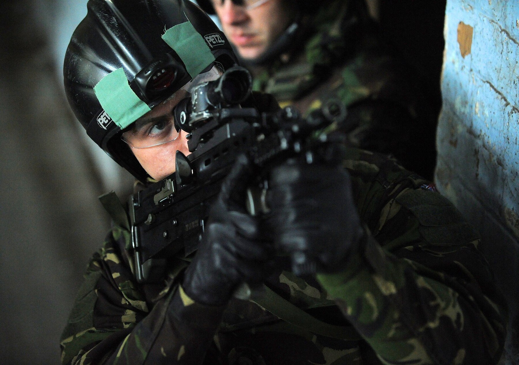 Figure 8 — A Royal Marine in close-quarter battle training on Exercise Seaspray, 2010, aiming an SA80 with an optical sight from a doorway; note the comma-shaped A2 cocking handle beside his cheek. Naval boar…