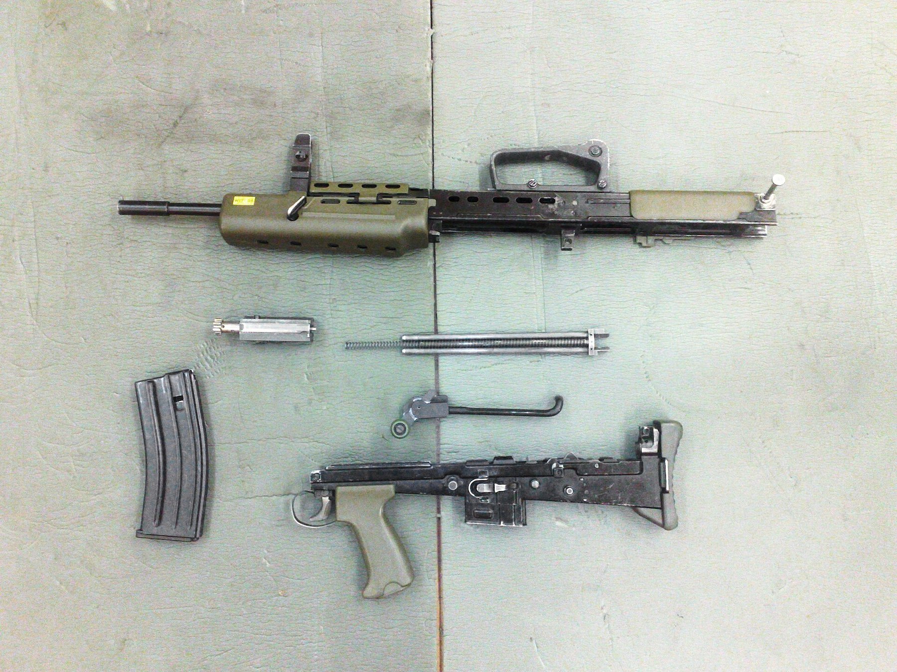 Figure 11 — An L98A1 cadet rifle stripped: the body and barrel with the external operating-rod track and its large cranked cocking lever, the trigger mechanism housing with the cadet pattern pistol grip, the b…