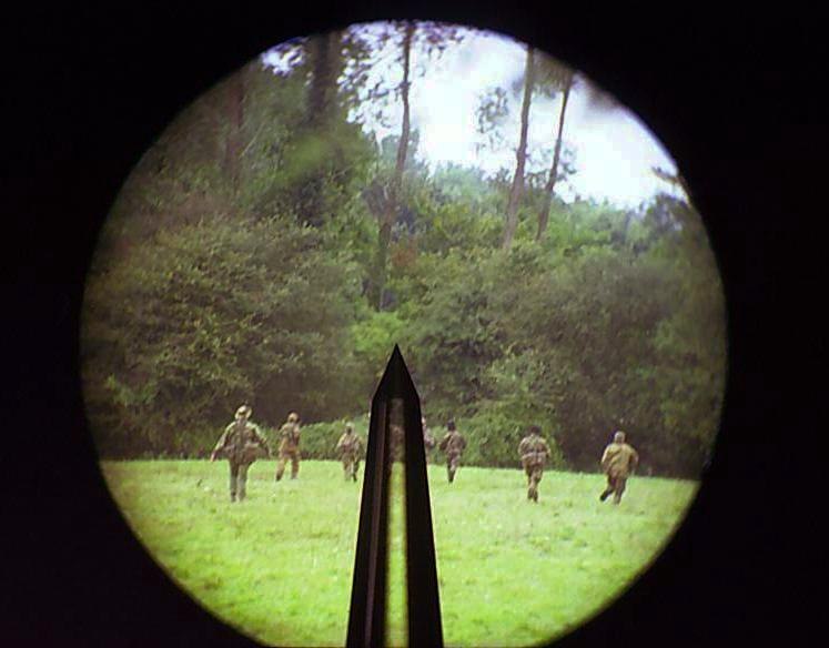 Figure 1 — The view through a SUSAT: the dark pillar pointer rising from the bottom of the circular field, with soldiers advancing across a field. Photograph by Strelivi, public domain, via Wikimedia Commons.