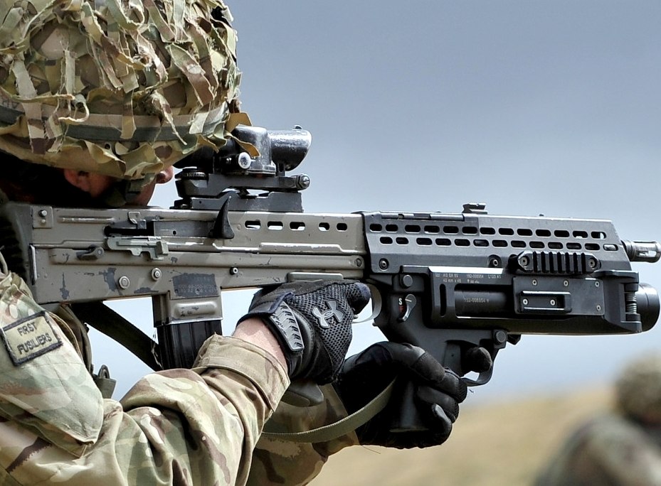 Figure 6 — A soldier of the First Fusiliers aims an L85A2 fitted with a SUSAT and the underslung grenade launcher, whose body replaces the handguard and is marked "AG SA 80" with an L123 designation. Original…