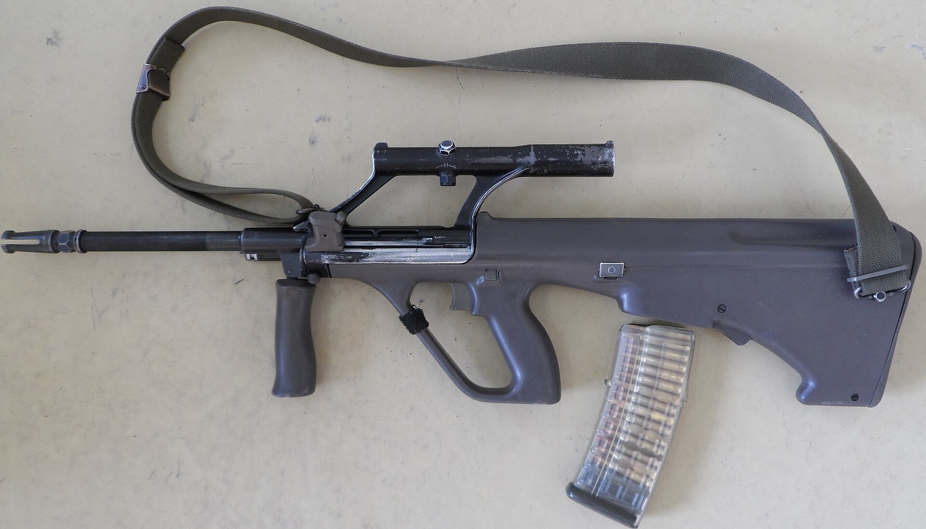 Figure 1 — An AUG with the integral optic, the pattern Austria issued as the StG 77, with a transparent 30-round magazine and the issue sling. Everything that made the rifle unusual in 1977 is visible: the bu…