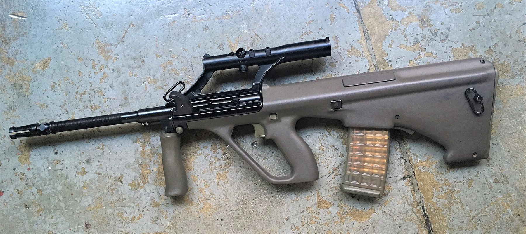 Figure 4 — An AUG in olive furniture with the 1.5× optic, identified by its uploader as an A2 with the detachable scope. The optic housing and the receiver are the same outline as on an A1; the difference is …