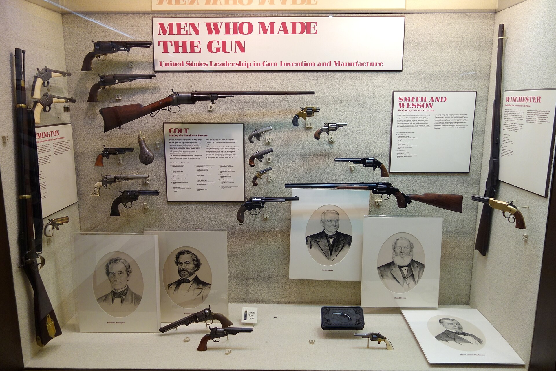 Figure 1 — A museum case at the Huntington Museum of Art, West Virginia, "Men Who Made the Gun". At right, under the Winchester panel, is a brass-framed Volcanic-type pistol beside a lever rifle; the Smith an…