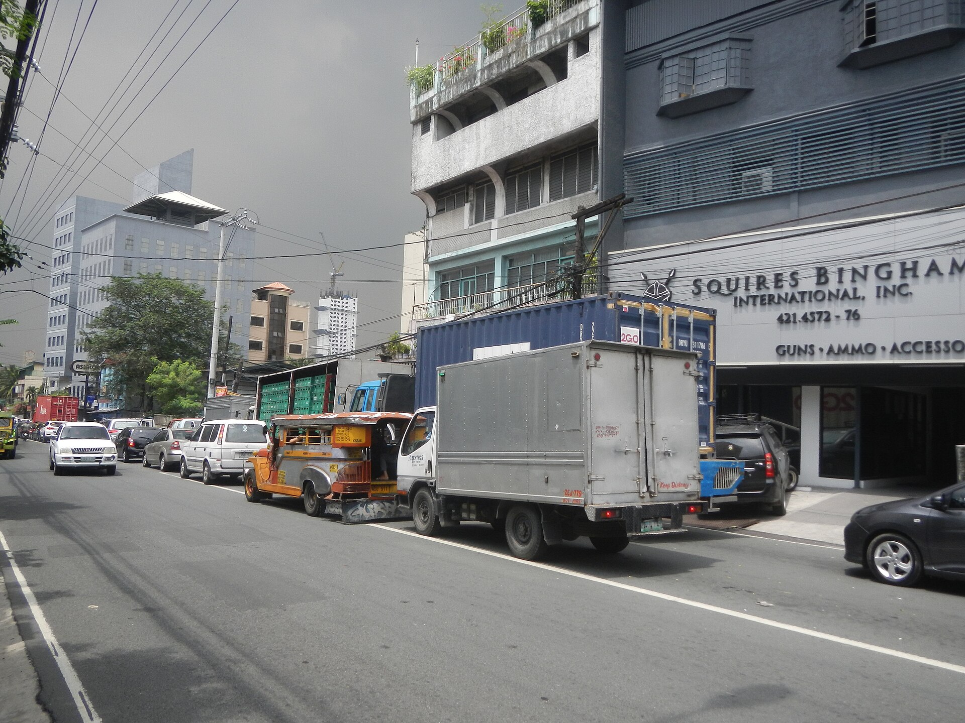 Figure 2 — A street view on Bonny Serrano Avenue, Cubao, Quezon City, with a multi-storey building at right carrying the sign "SQUIRES BINGHAM INTERNATIONAL, INC. — GUNS · AMMO · ACCESSORIES". The photograph …