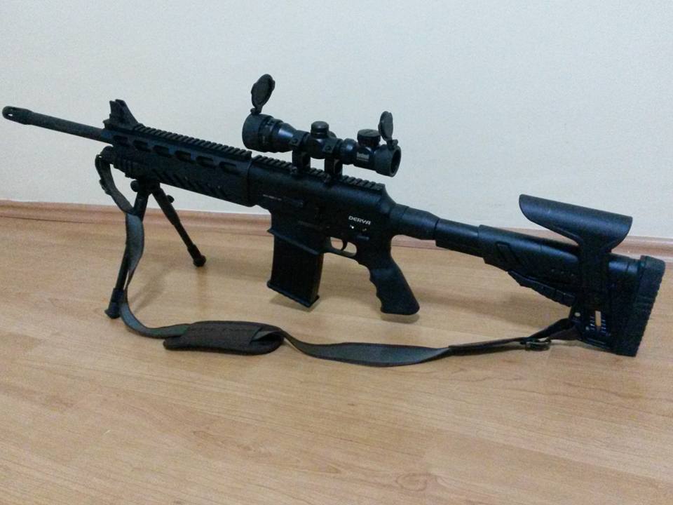 Figure 2 — A Derya MK-10 fitted, in its uploader's words, with a Picatinny rail, a bipod and a telescopic sight, resting on a wooden floor. The MK-10 is another of Derya's box-fed shotguns: the thumbhole-styl…
