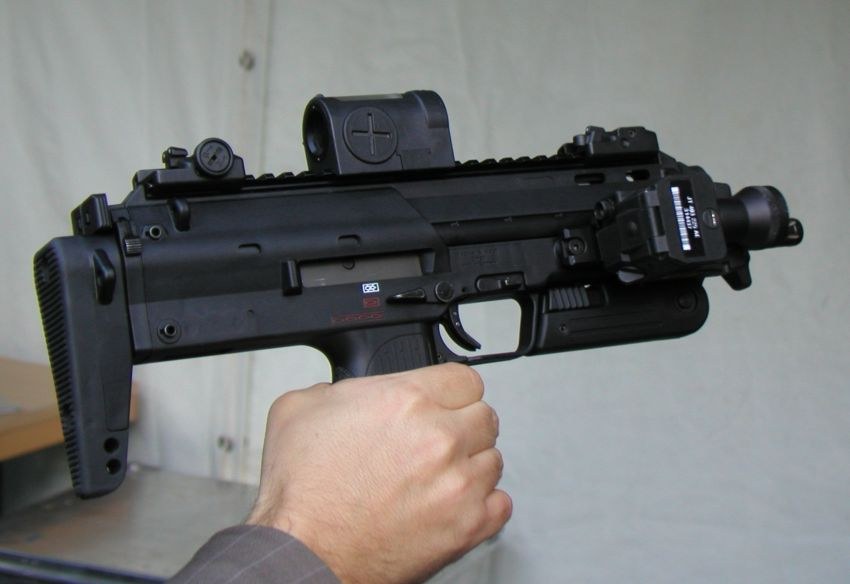 Figure 7 — An MP7 photographed in September 2006, right side, with a reflex sight and a laser-light module on the right-side rail, held by the grip. The stock's straight butt plate and the side rail ahead of …