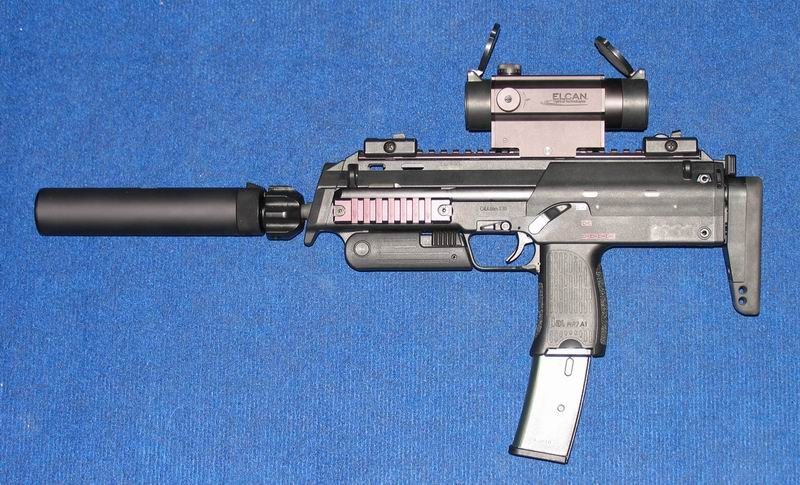 Figure 6 — An MP7A1 from the left side, fitted with H&K's suppressor, an ELCAN optic on the top rail and a translucent 40-round magazine. The left side carries no ejection port; the selector and the H&K grip …