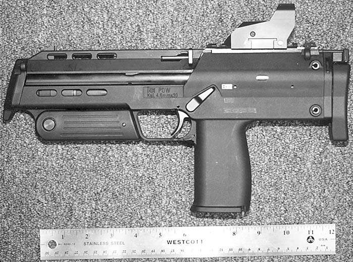 Figure 2 — The HK PDW prototype as Small Arms Review photographed it in 2000, with its stock and vertical foregrip stowed, beside a 12-inch rule. The receiver is marked "HK PDW, Kal. 4.6mm x 30"; the grip is …