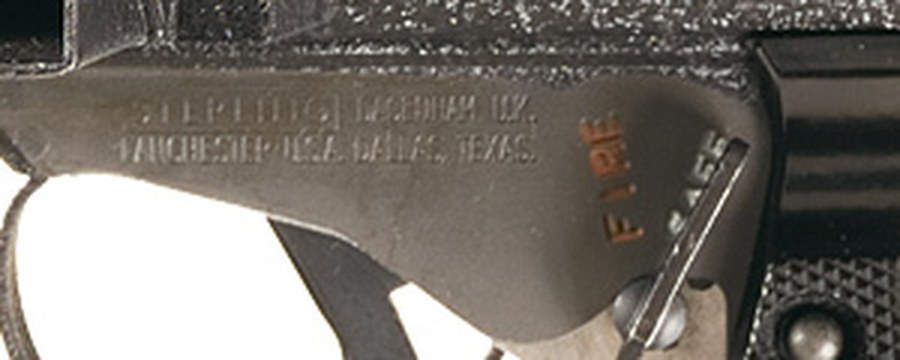 Figure 2 — Left side of the trigger housing of a Mark 7 C4: "STERLING DAGENHAM U.K." over "LANCHESTER U.S.A. DALLAS, TEXAS", and the change lever's two positions, FIRE (in red) and SAFE. Enlarged three times …